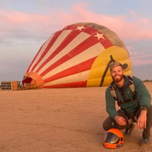 Noah Boswell crouching in front of a hot air balloon